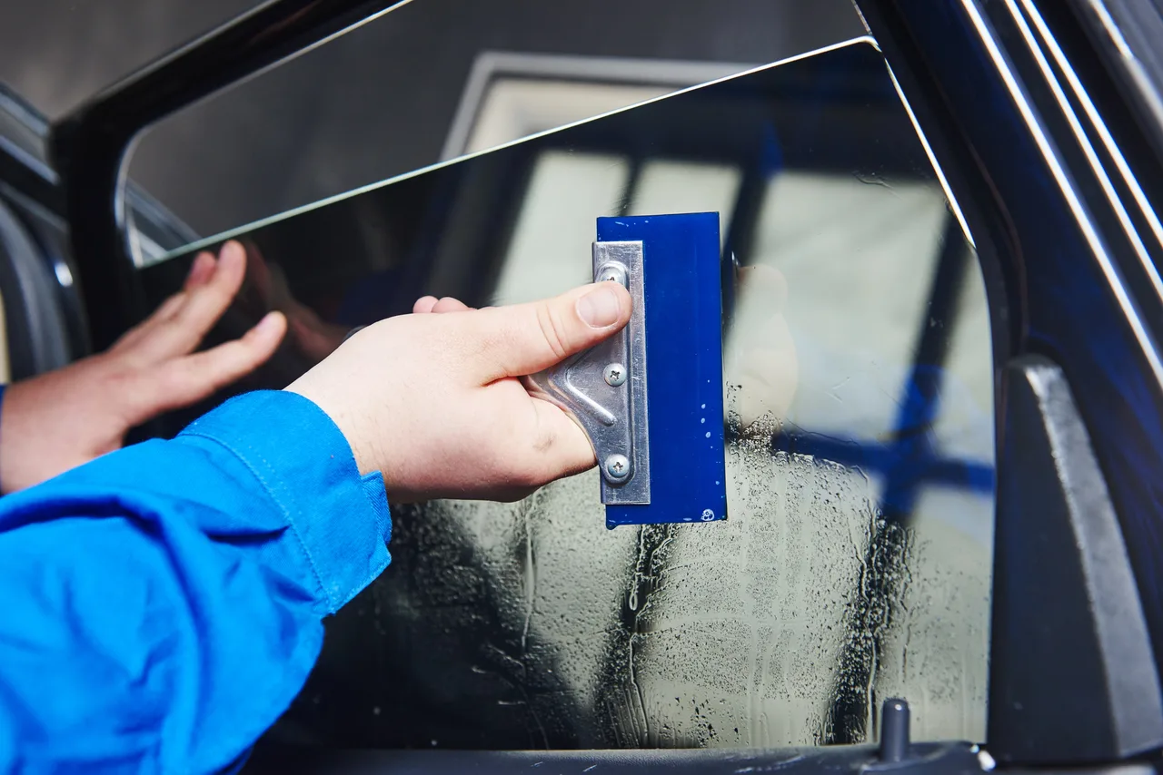 Hands smoothing tint film onto a car window with a blue squeegee.